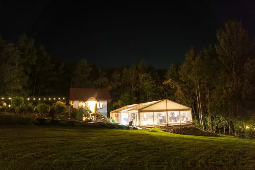Anielsko nocą – dom i namiot w światłach nad trawnikiem